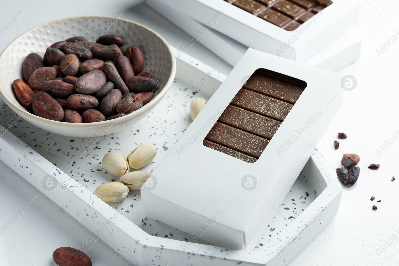 Photo of Tasty Dubai chocolate bar in package with pistachios, knafeh and cocoa beans on white textured table, closeup. Space for text