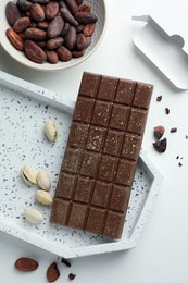 Photo of Tasty Dubai chocolate bar with pistachios, knafeh and cocoa beans on white textured table, flat lay