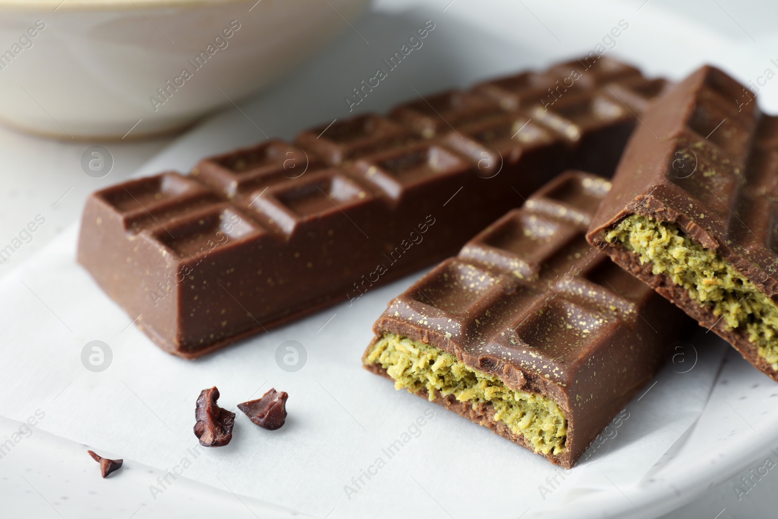 Photo of Tasty Dubai chocolate bars with pistachios and knafeh on plate, closeup