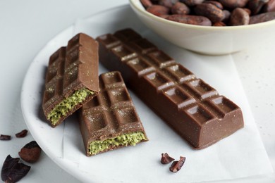 Tasty Dubai chocolate bars with pistachios, knafeh and cocoa beans on light table, closeup