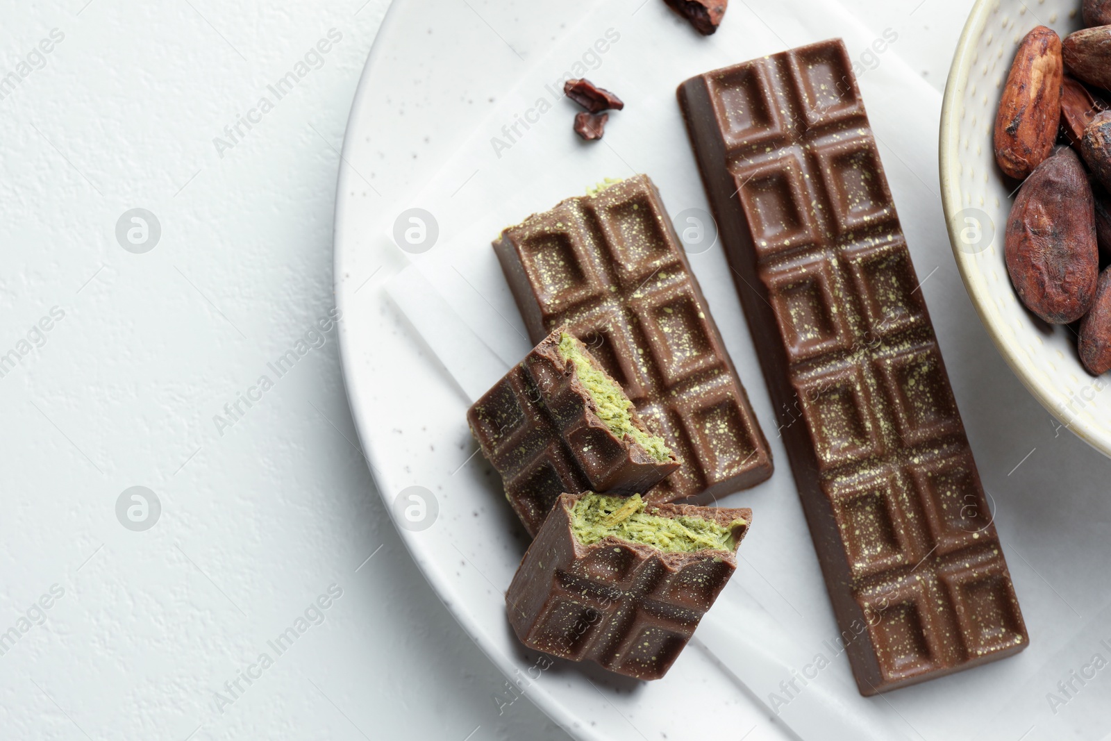 Photo of Tasty Dubai chocolate bars with pistachios, knafeh and cocoa beans on white textured table, top view. Space for text