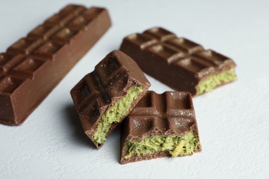 Pieces of tasty Dubai chocolate with pistachios and knafeh on white textured table, closeup