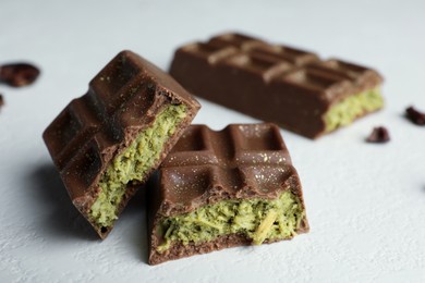 Pieces of tasty Dubai chocolate with pistachios and knafeh on white textured table, closeup