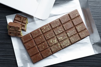 Photo of Tasty Dubai chocolate with pistachios and knafeh on black wooden table, top view