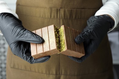 Photo of Woman breaking tasty Dubai chocolate with pistachios and knafeh indoors, closeup