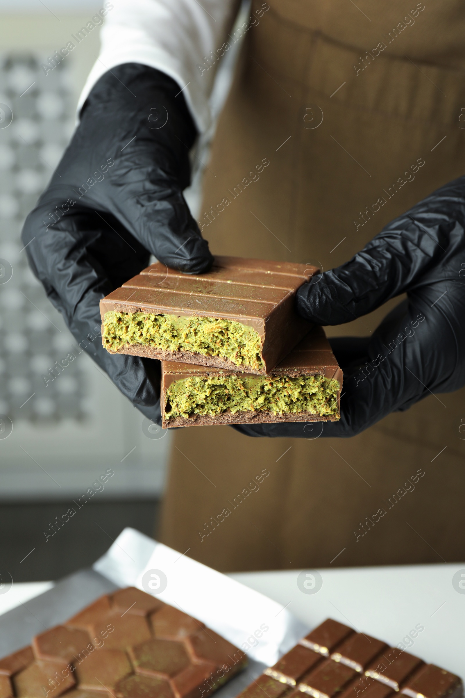 Photo of Woman holding pieces of tasty Dubai chocolate with pistachios and knafeh at table indoors, closeup