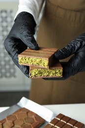 Photo of Woman holding pieces of tasty Dubai chocolate with pistachios and knafeh at table indoors, closeup