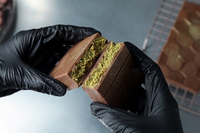 Woman breaking tasty Dubai chocolate with pistachios and knafeh at grey table, closeup