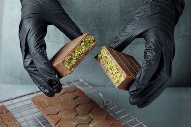 Woman breaking tasty Dubai chocolate with pistachios and knafeh at grey table, closeup