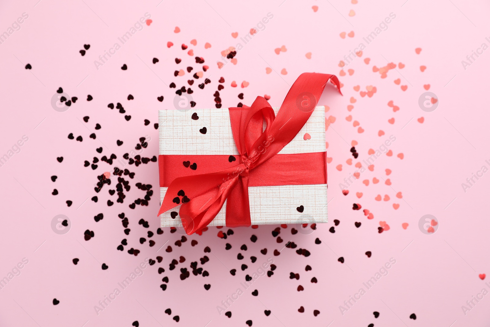 Photo of Romantic gift and confetti on light pink background, top view