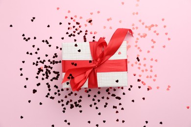 Romantic gift and confetti on light pink background, top view