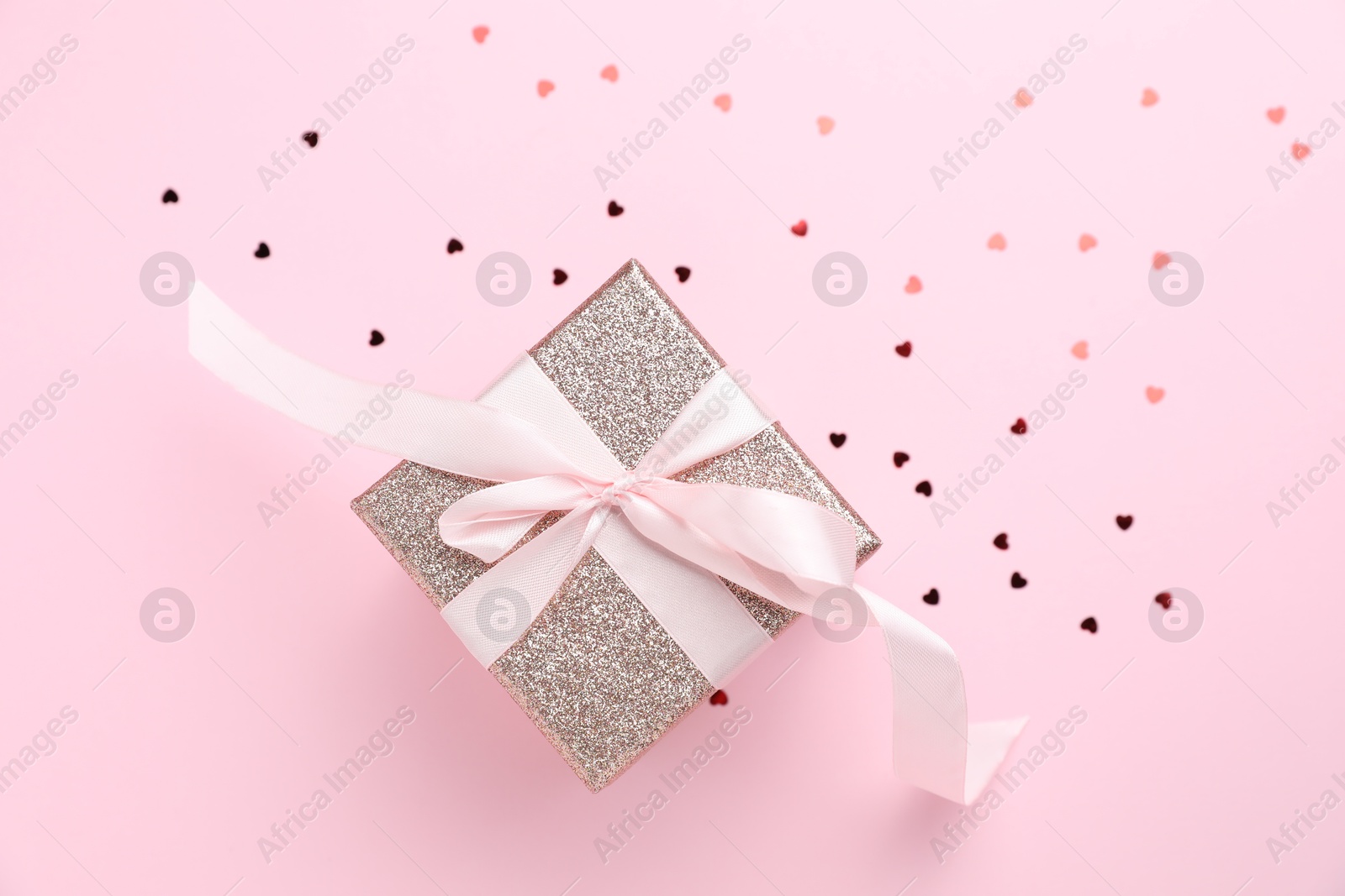 Photo of Romantic gift and confetti on light pink background, top view