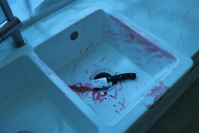 Photo of Knife and sink smeared in blood indoors. Crime scene