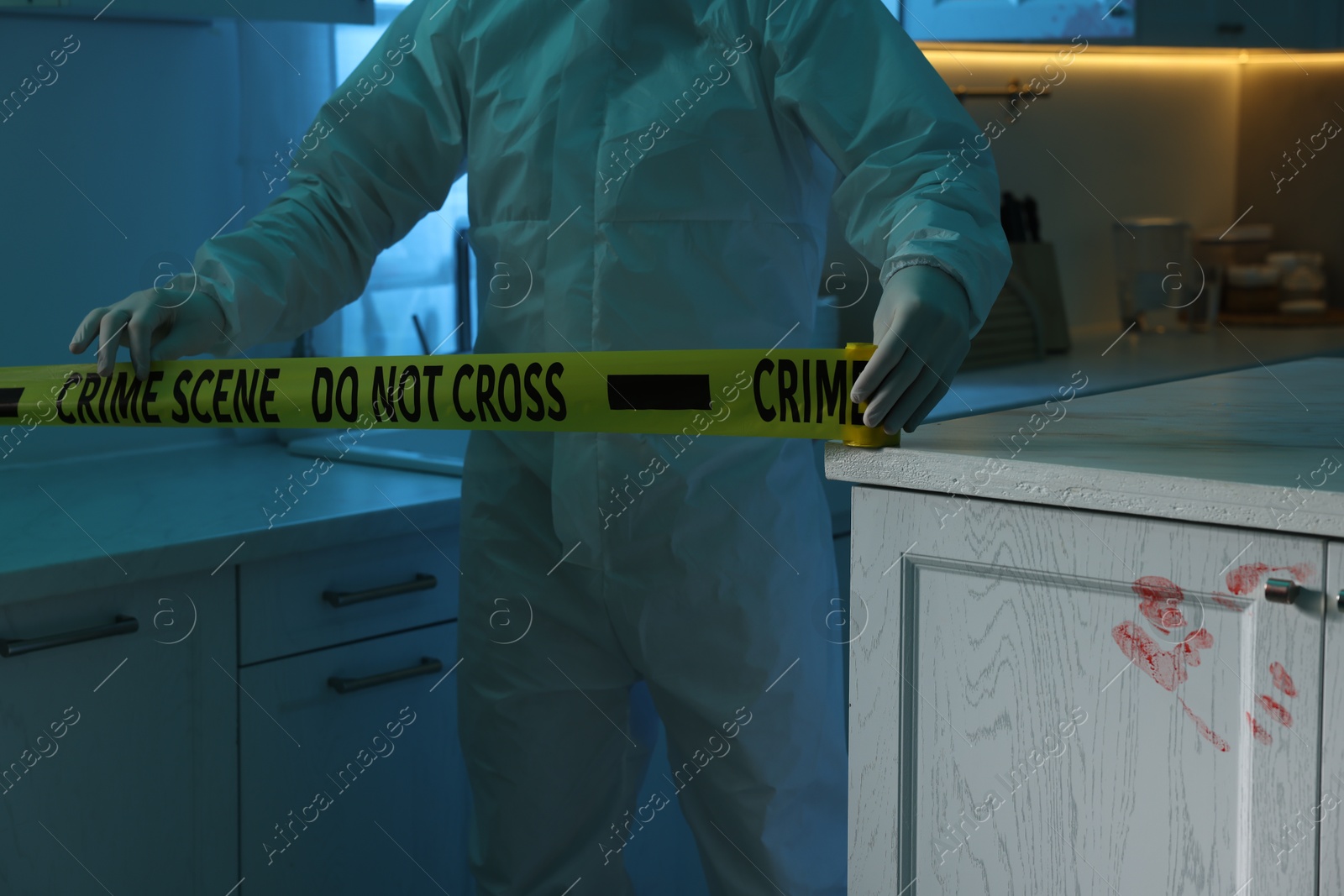 Photo of Forensic expert blocking way to crime scene with yellow tape indoors, closeup