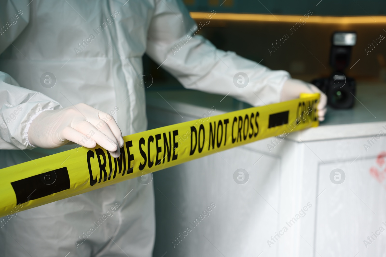 Photo of Forensic expert blocking way to crime scene with yellow tape indoors, closeup