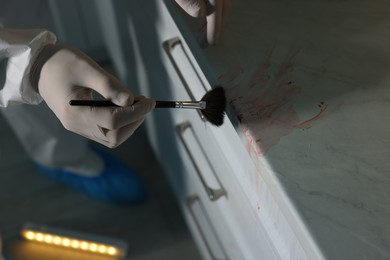 Photo of Forensic expert taking fingerprints from countertop with brush at crime scene indoors, closeup