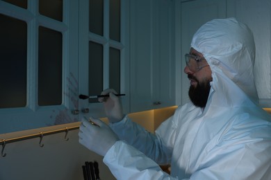 Photo of Forensic expert taking fingerprints from cupboard with brush at crime scene indoors