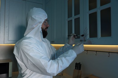 Photo of Forensic expert taking fingerprints from cupboard with brush at crime scene indoors