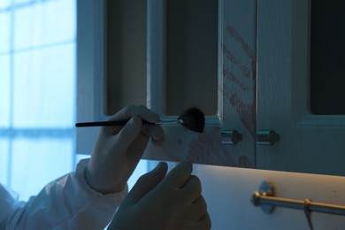 Photo of Forensic expert taking fingerprints from cupboard with brush at crime scene indoors, closeup