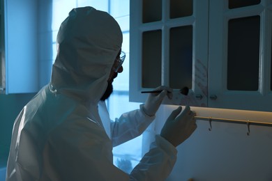 Photo of Forensic expert taking fingerprints from cupboard with brush at crime scene indoors