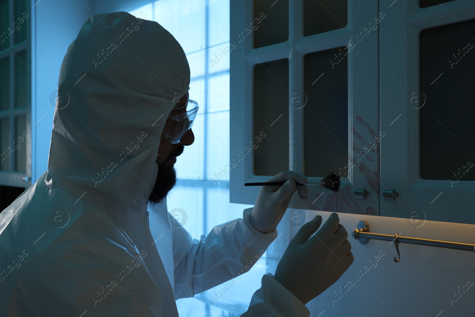 Photo of Forensic expert taking fingerprints from cupboard with brush at crime scene indoors