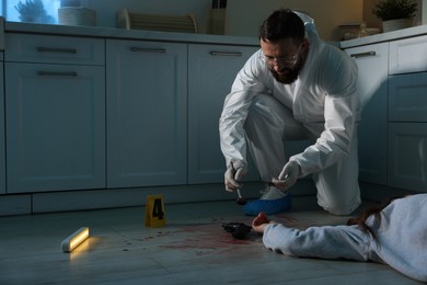 Photo of Forensic expert taking fingerprints with brush from gun and dead body at crime scene indoors