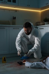 Photo of Forensic expert taking fingerprints with brush from gun and dead body at crime scene indoors