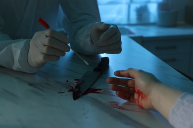 Photo of Forensic expert taking blood sample and dead woman's body at countertop indoors, closeup