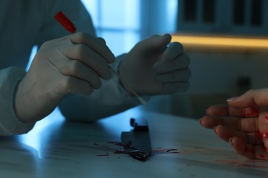 Photo of Forensic expert taking blood sample and dead woman's body at countertop indoors, closeup