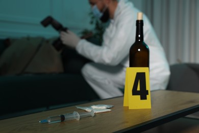 Photo of Forensic expert with camera working at crime scene indoors, focus on drugs and bottle of wine