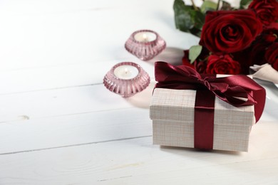 Romantic gift, roses and burning candles on white wooden table, closeup. Space for text