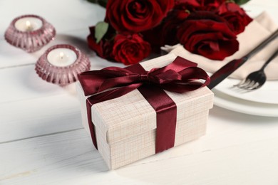 Photo of Beautiful table setting with romantic gift, flowers and burning candles on white wooden background, closeup