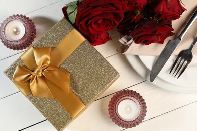 Photo of Beautiful table setting with romantic gift, flowers and burning candles on white wooden background, flat lay