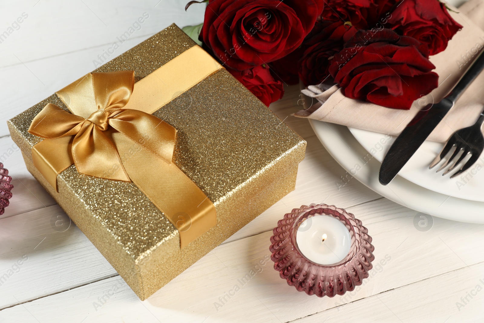 Photo of Beautiful table setting with romantic gift, flowers and burning candle on white wooden background, closeup