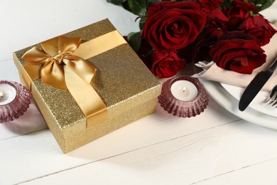 Photo of Beautiful table setting with romantic gift, flowers and burning candles on white wooden background, closeup