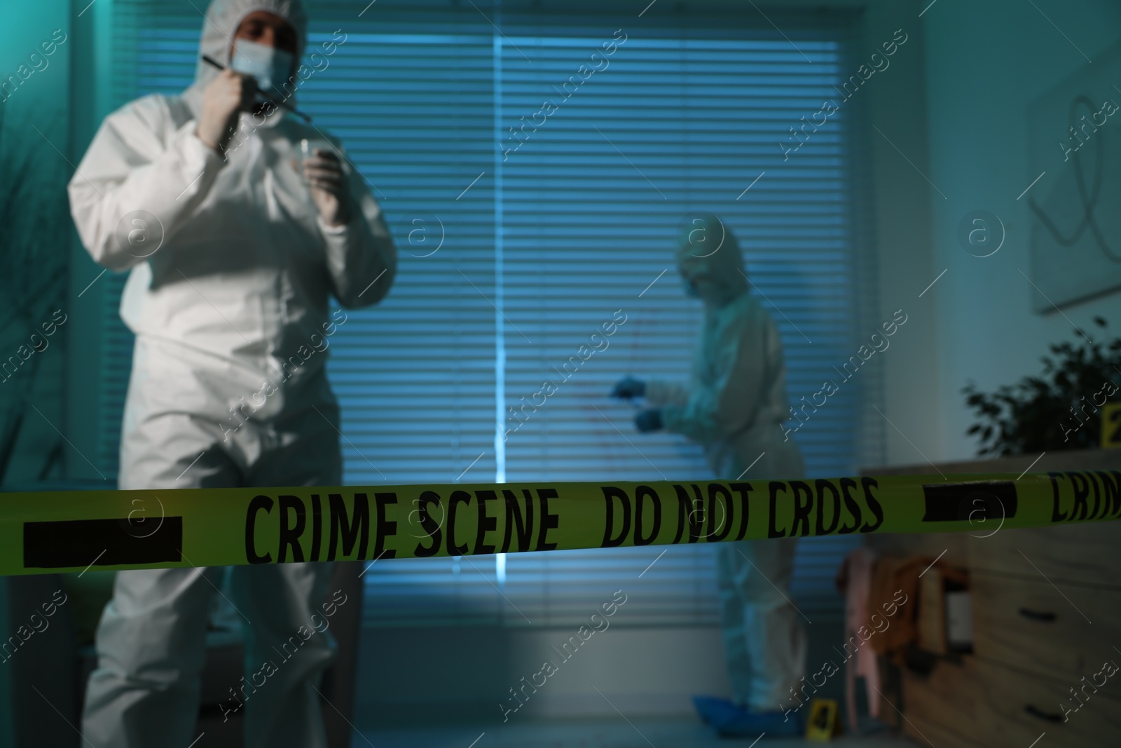 Photo of Forensic experts working at crime scene indoors, focus on yellow tape