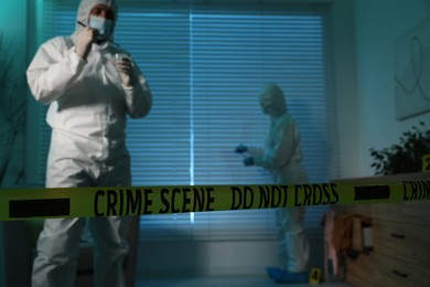 Photo of Forensic experts working at crime scene indoors, focus on yellow tape