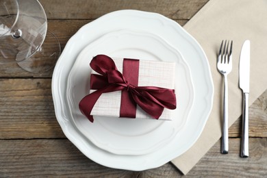 Beautiful table setting with romantic gift on wooden background, flat lay