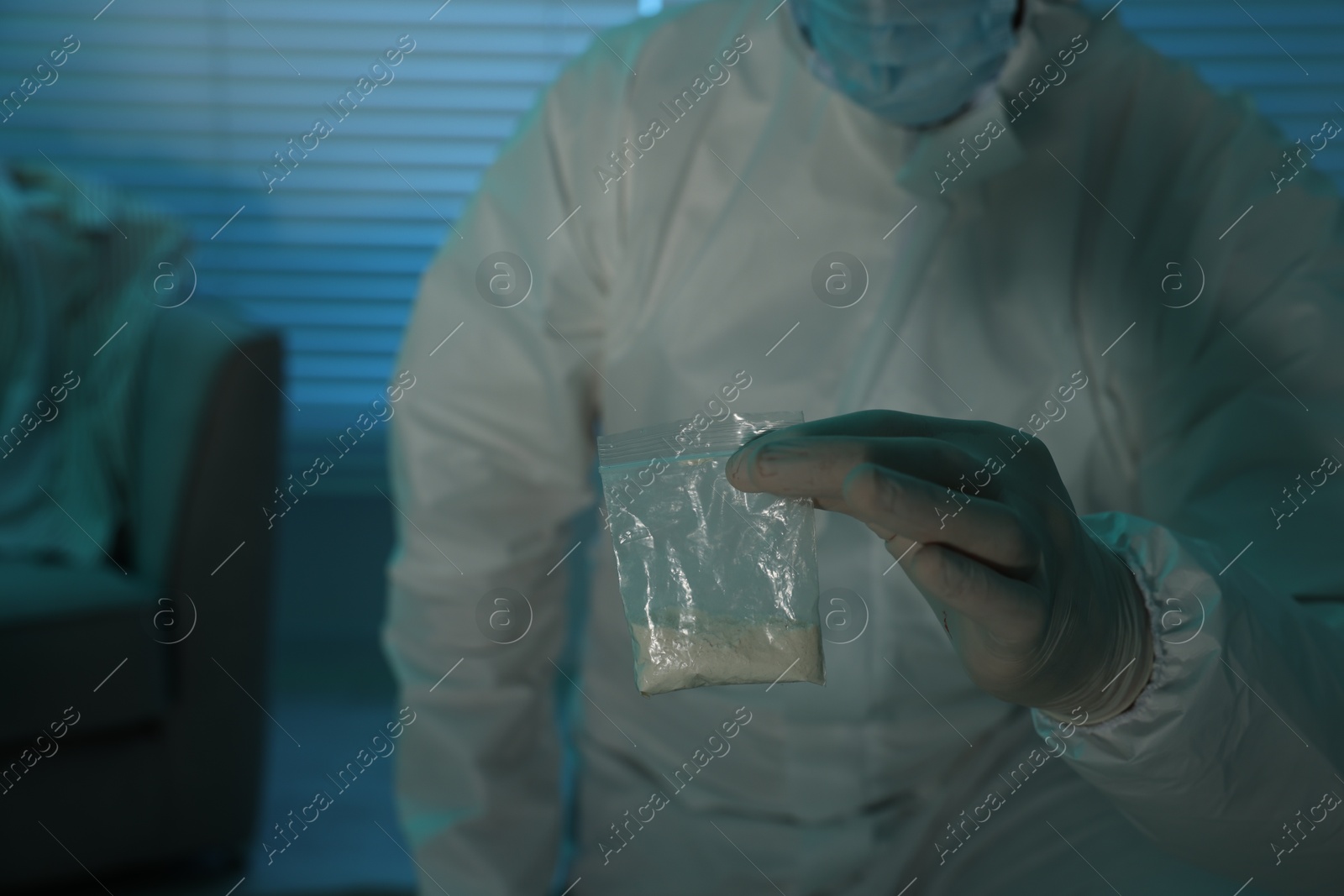 Photo of Forensic expert holding plastic bag with drug powder indoors, closeup