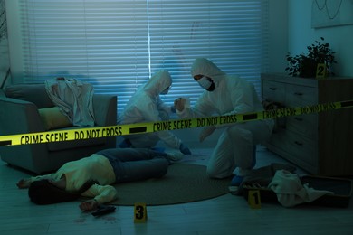 Photo of Forensic experts working at crime scene with dead woman's body indoors