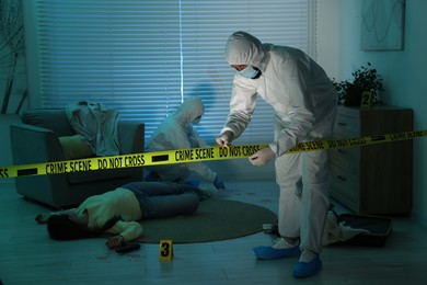 Photo of Forensic experts working at crime scene with dead woman's body indoors