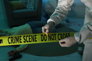 Photo of Forensic expert with yellow crime scene tape and dead woman's body indoors, closeup