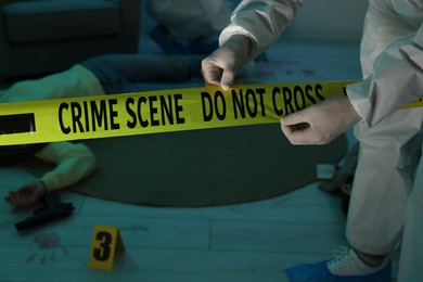 Photo of Forensic expert with yellow crime scene tape and dead woman's body indoors, closeup