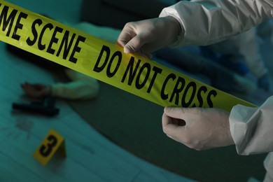 Photo of Forensic expert with yellow crime scene tape and dead woman's body indoors, closeup