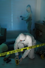 Forensic experts working at crime scene with dead woman's body indoors