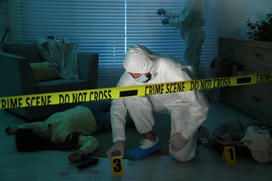 Forensic experts working at crime scene with dead woman's body indoors