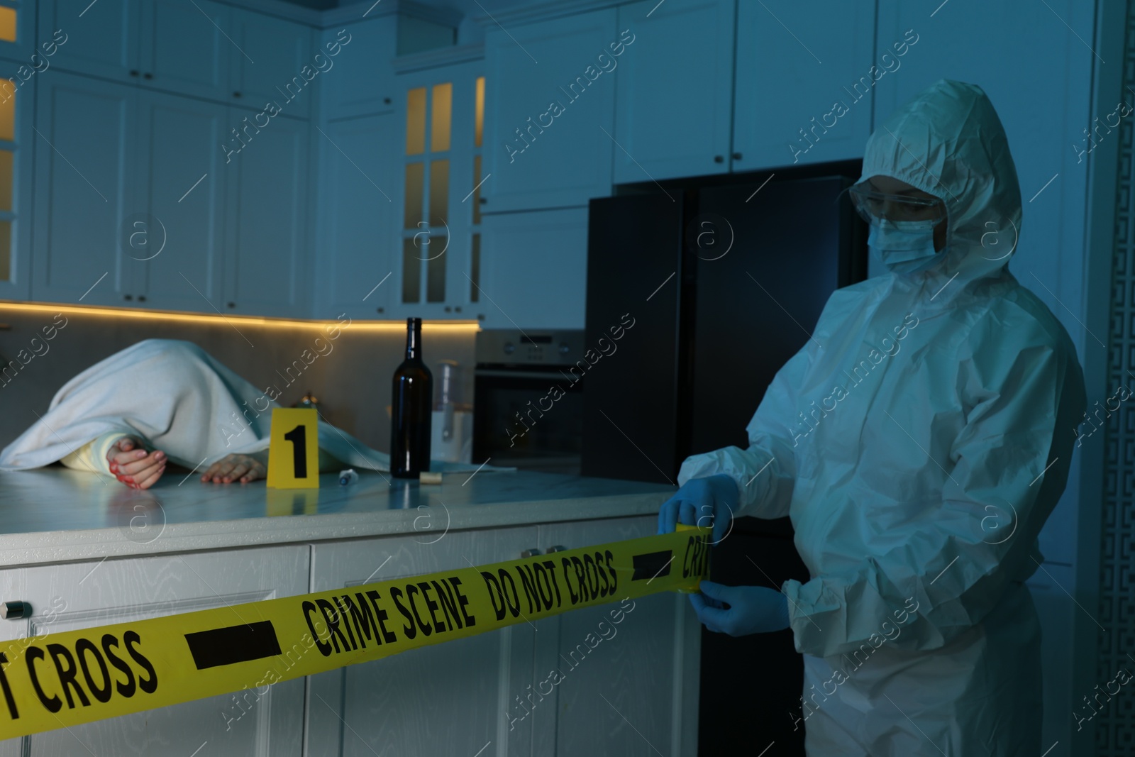 Photo of Forensic expert blocking way to crime scene and dead body with yellow tape indoors