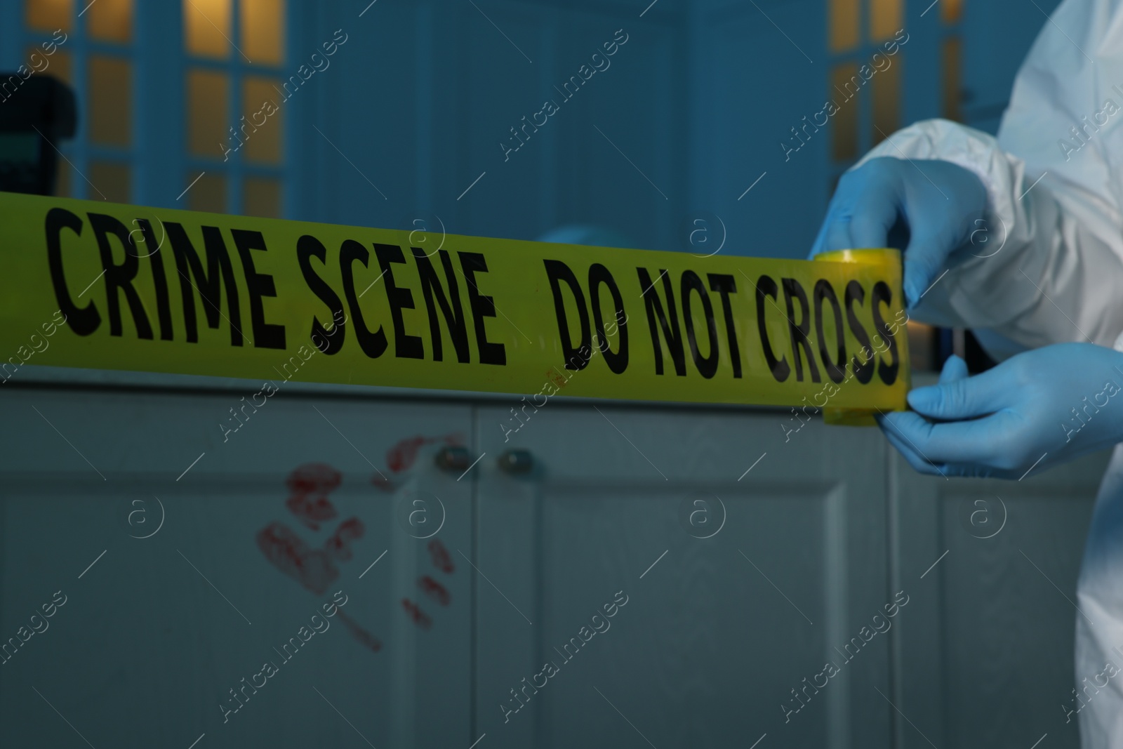 Photo of Forensic expert blocking way to crime scene with yellow tape indoors, closeup