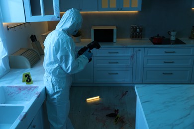 Forensic expert with camera working at crime scene in dark room