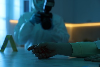 Photo of Forensic expert with camera working at crime scene and dead woman's body indoors, selective focus